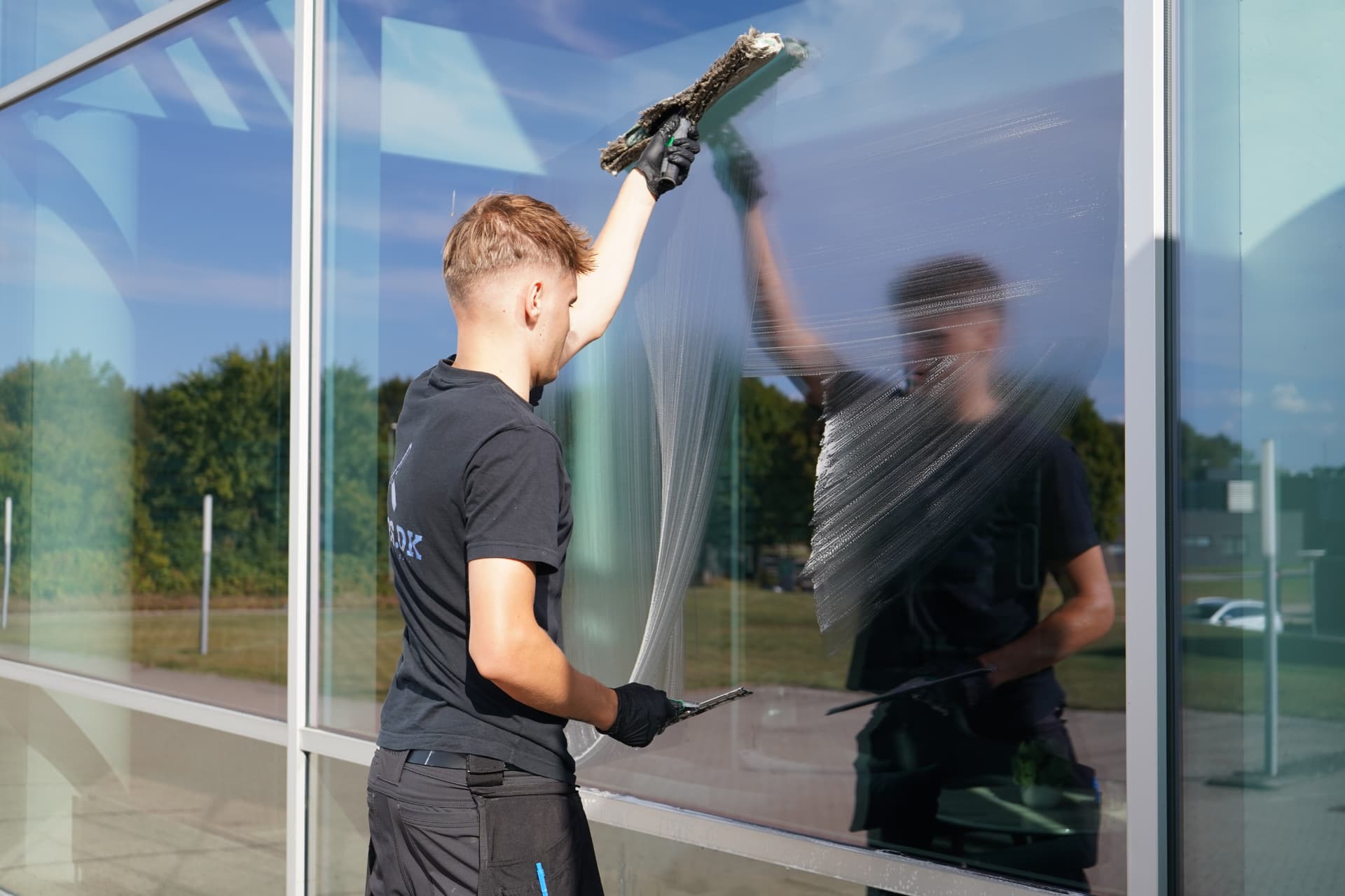Vinduespudser i gang med skraber på stor glasfacade